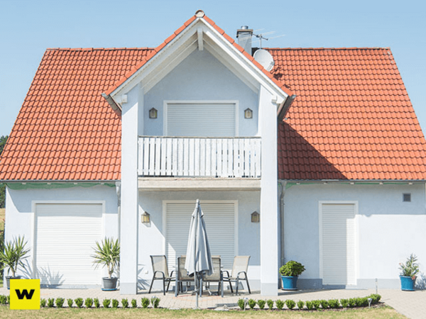 Modernes Einfamilienhaus mit rotem Satteldach, geschlossenem Balkon und Gartenmöbeln.